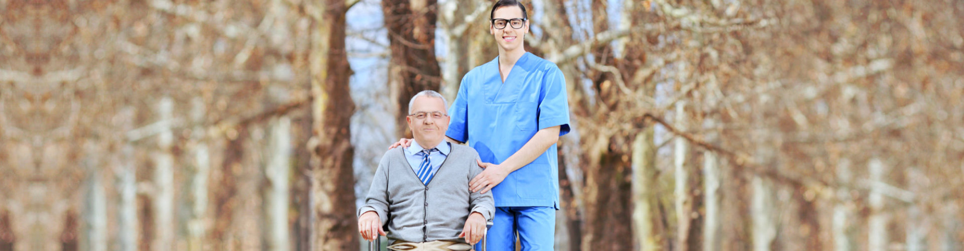 caregiver wearing eye glasses and senior man sitting in the wheelchair smiling